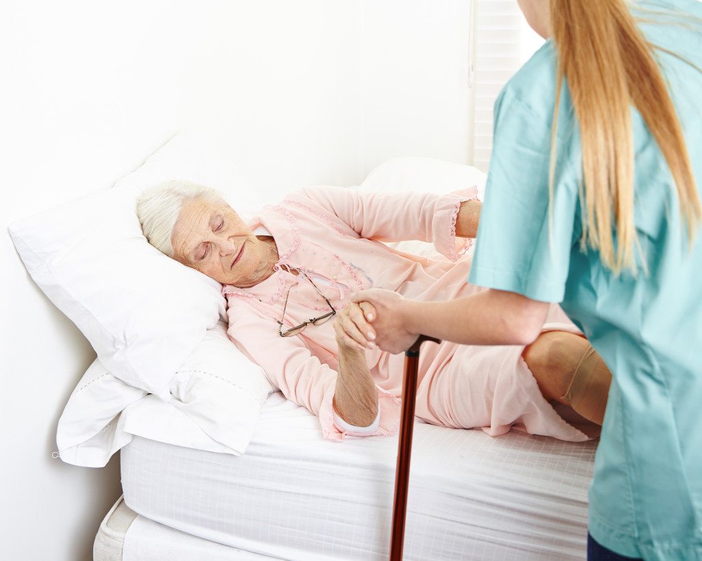 Caregiver helping senior woman in nursing home out of bed